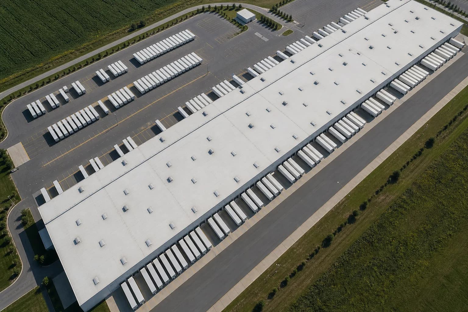 An aerial view of a large logistics hub with dozens of loading dock doors and trailers backed onto the docks
